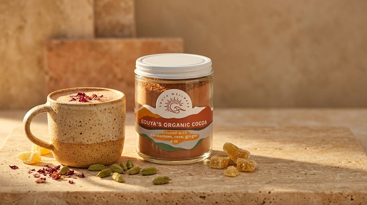 Gouya cocoa jar beside a ceramic mug of cocoa on a stone surface with cardamom pods and ginger pieces